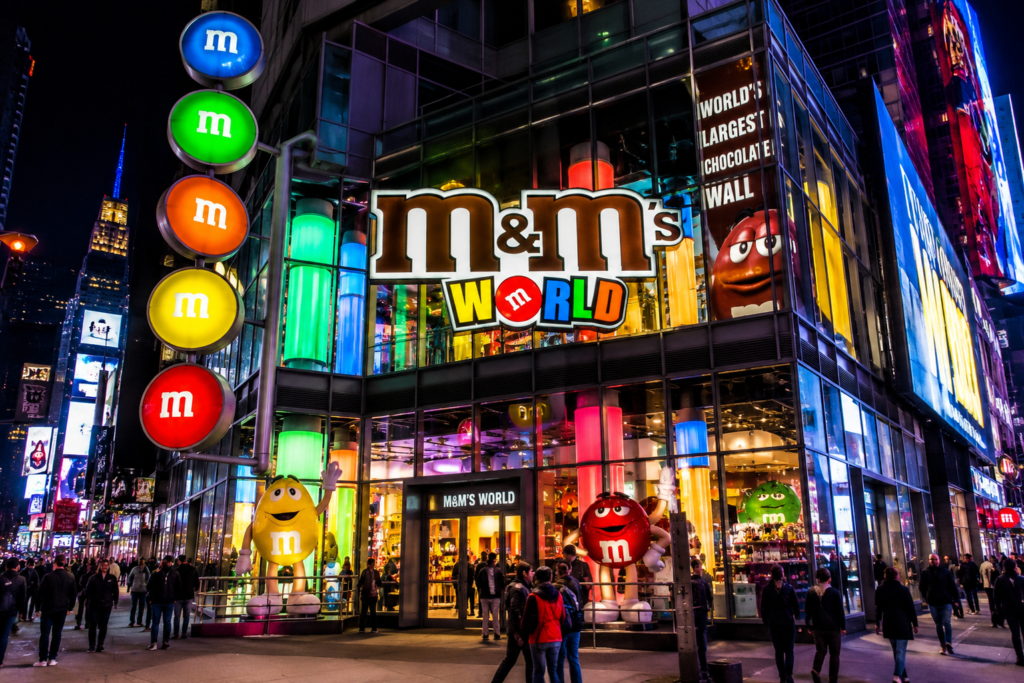 M&M'S World flagship store in Times Square, New York City, featuring colorful M&M characters, bright LED displays, and visitors at the entrance.